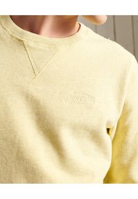Felpa gialla realizzata in morbido tessuto, con scollo a costine e un sottile logo ricamato sul petto.