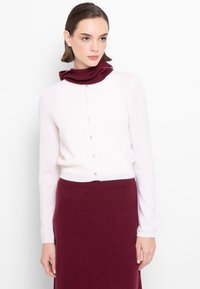 Jasnoróżowy kardigan z burgundowym kołnierzem, z przodu na guziki i długimi rękawami. Materiał wydaje się miękki i o fakturze.