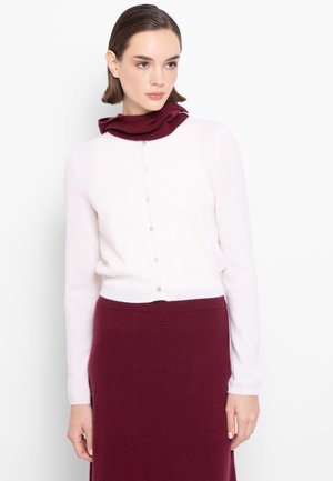 Cardigan rosa chiaro con collo a lupetto bordeaux, dotato di chiusura a bottoni e maniche lunghe. Il tessuto sembra morbido e testurizzato.