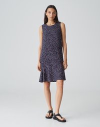 Mouwloze jurk met een uitlopende zoom, met een marineblauwe achtergrond en kleine, kleurrijke stippatronen. Draag het met zwarte sandalen.