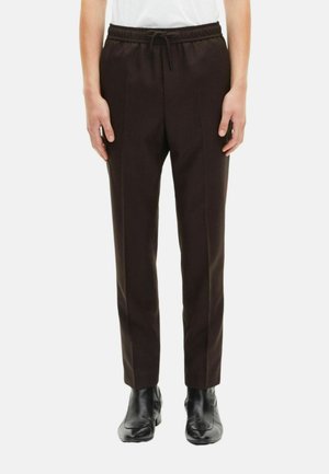 Pantaloni marroni slim-fit con vita elastica e cordino, caratterizzati da pieghe laterali e una texture liscia, abbinati a stivali neri.