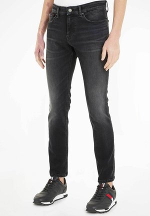 Jeans de mezclilla negra con un corte ajustado, que presentan cinco bolsillos, cierre de botón y un ligero desvanecimiento. Combinados con zapatillas deportivas negras.