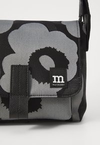 Black and gray fabric bag featuring a floral pattern, rectangular shape, flap closure, and a small branded tag with "marimekko."