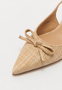 Auduma salmu siksnu kurpes gaiši bēšā krāsā ar norādītu purngalu un lentītes akcentu priekšpusē. Gluda iekšējā odere, minimālistisks dizains.