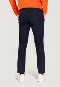 Chinos blu navy con vestibilità slim, dotati di tasche posteriori, tasche laterali e una texture sottile. Abbinati a sneakers bianche e un maglione arancione.