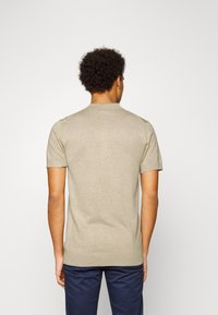 Beige stickad polo med korta ärmar och ribbad krage, bärs med marinblå byxor. Tyget verkar mjukt och lätt.