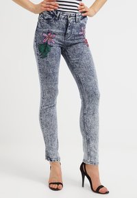 Jasnoniebieskie jeansy rurki z kwiatowym haftem w różowym i zielonym na przodzie, z wyblakłym wykończeniem i dopasowanym krojem.