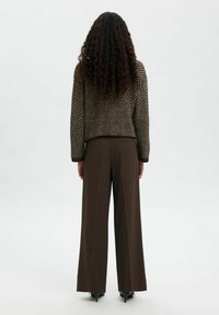 Svetr s hnědým houndstooth vzorem a volným střihem, zkombinovaný s hnědými kalhotami s vysokým pasem a širokými nohavicemi, a černými botami.