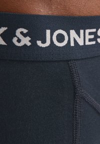 Marineblauwe onderbroek met een zachte elastische tailleband met de merknaam "K & JONES" in lichtgrijze letters. Gladde, gestructureerde stof.