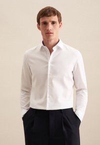 Witte overhemden met een textuur, voorzien van een klassieke kraag en lange mouwen. Gecombineerd met donkere geplooide broek.