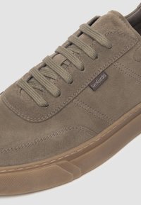Sneaker in suede marrone con punta rotonda, lacci verde oliva e suola in gomma. Presenta cuciture sottili e un piccolo etichetta con logo sul lato.