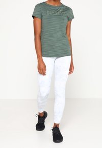 Grönrandig t-shirt med kort ärm med texten "CROSSFIT", tillsammans med vita leggings med marmormönster och svarta träningsskor.