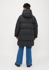 Black padded coat with a hood, featuring a boxy design and ribbed texture. Worn over blue flared jeans and chunky black boots.