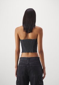 Svart denim strapless korsettop med texturerad tyg, som har en åtsittande design och en kortad längd. Kombineras med hög midja svarta cargobyxor.