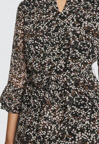 Sukienka z szyfonu na czarnym tle, zdobiona wielokolorowym, cętkowanym wzorem w odcieniach różu, beżu i brązu. Posiada talię z marszczeniem oraz falbaniaste rękawy.