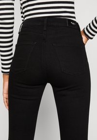 Mustat korkea vyötäröiset farkut, joissa on sileä denimi pinta, takataskut ja hillityt ommeltu yksityiskohdat. Yhdistetty raidalliseen pitkähihjaiseen paitaan.