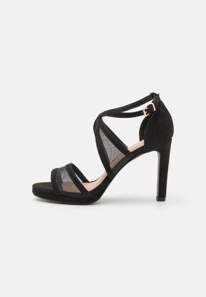 Black high-heeled sandal featuring a combination of soft suede and mesh panels, with crisscross straps and an ankle buckle.