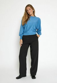 Maglione azzurro chiaro con maniche lunghe abbinato a pantaloni neri a gamba larga. Il maglione presenta un orlo a coste; i pantaloni hanno tasche e una texture liscia.