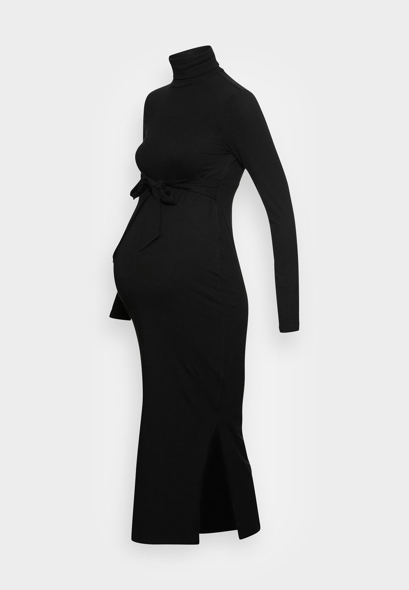 Robe de maternité noire à manches longues, longueur genou, col roulé et ceinture nouée à la taille, fente latérale sur fond clair uni.