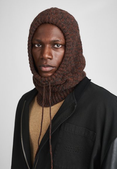 Cappuccio lavorato a maglia marrone e grigio con un motivo testurizzato, dotato di un cordino. Indossato con una maglietta beige e una giacca nera con zip.