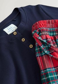 Dunkelblaues Langarmshirt mit gerippter Textur und zwei Holzknöpfen, kombiniert mit roten und grünen karierten Pyjamahosen mit einem elastischen Bund.