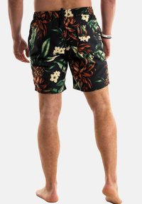Pantaloni da bagno neri con un vivace motivo tropicale di foglie e fiori. Vita elastica e lunghezza sopra il ginocchio.