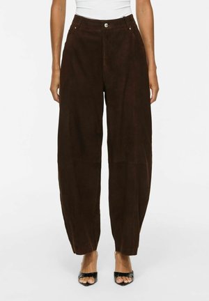 Pantalon marron foncé à jambe droite avec poches avant, porté par une personne portant des talons noirs ouverts à l'avant et un haut blanc court à la taille.