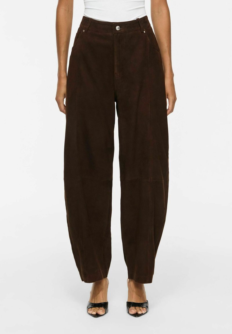 Pantalon marron foncé à jambe droite avec poches avant, porté par une personne portant des talons noirs ouverts à l'avant et un haut blanc court à la taille.
