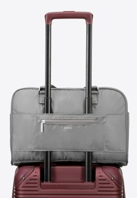 Sac de voyage gris avec une surface texturée, poche frontale zippée et double poignée rétractable noire, monté sur une valise rigide bordeaux.