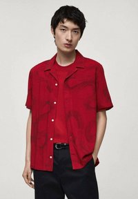 Rode shirt met korte mouwen en een subtiel abstract patroon, gecombineerd met een bijpassend rood T-shirt met ronde hals en zwarte broek.