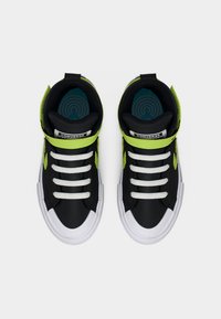 Μαύρα και νέον πράσινα ψηλά αθλητικά παπούτσια Converse με λευκά κορδόνια και σόλες, φωτογραφημένα από πάνω σε απλό φόντο.