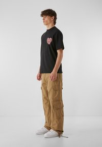 Svart bomull t-shirt med en röd hjärtgrafik, matchad med beige cargobyxor med flera fickor och vita sneakers.
