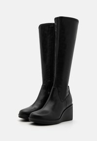 Botas negras hasta la rodilla hechas de cuero suave, con suela de cuña y cremallera lateral. Diseño sencillo con acentos mínimos.