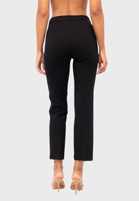 Hoge zwarte broeken met een slim fit, voorzien van een gladde textuur en een enkel-lengte ontwerp, gecombineerd met sandalen met een doorzichtige hak.