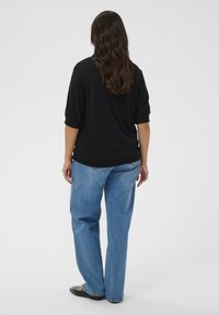 Czarny sweter z dzianiny z rękawami do trzech czwartych, zestawiony z jasnoniebieskimi spodniami typu wide-leg. Całość dopełniają czarne baleriny.