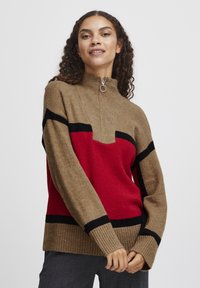 Strickpullover mit Reißverschlusskragen, in Khaki mit roten und schwarzen geometrischen Mustern. Der Stoff hat eine weiche Textur und gerippte Bündchen.