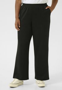 Pantalons de survêtement larges noirs avec une taille élastique et des poches latérales, fabriqués à partir d'un tissu doux, associés à des baskets ivoire.