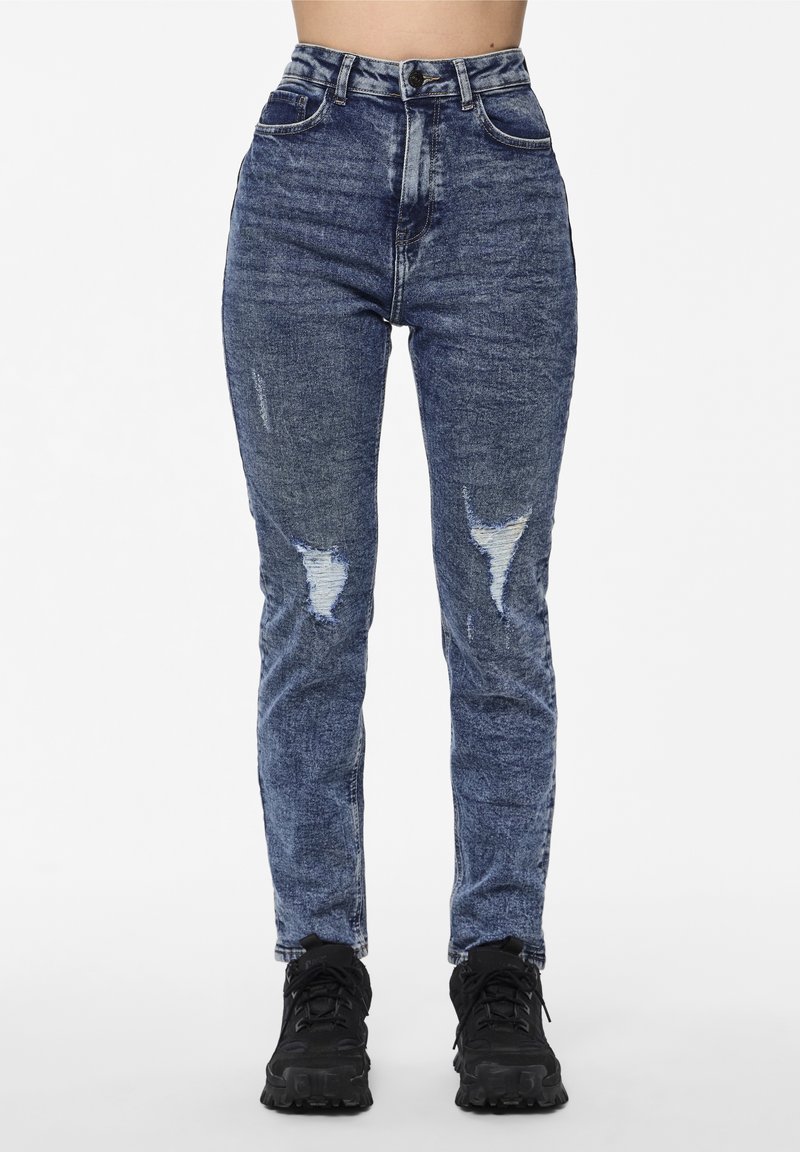 Jean denim bleu taille haute avec des zones usées, présentant une coupe droite et un léger délavé, assorti à des baskets noires.