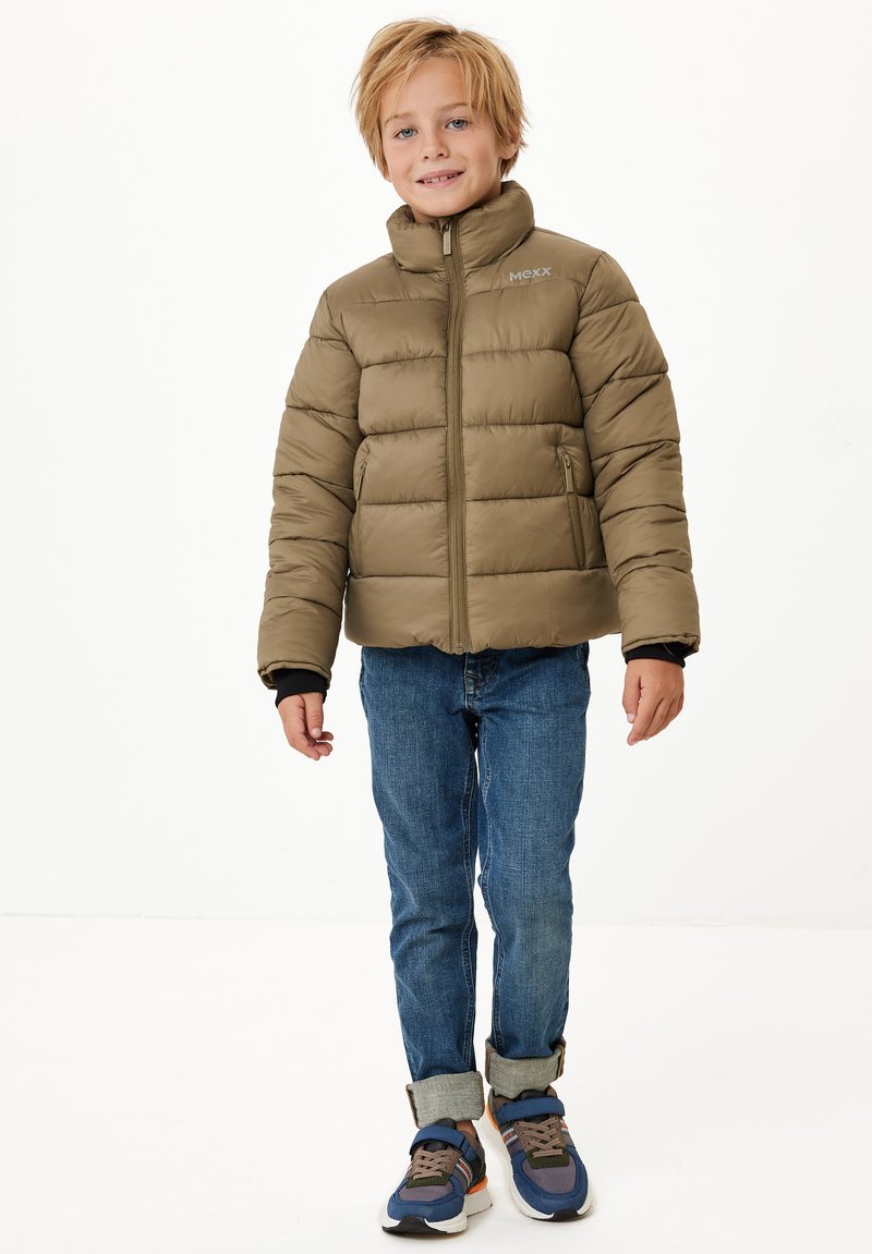 Olivgrön puffjacka med ståkrage och dragkedjefickor, bärs över en svart tröja och blå jeans, kompletterad med blå sneakers.