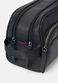 Black leather toiletry bag with dual zippers, sleek rounded shape, textile strap, and small colorful tag detail. Smooth texture.