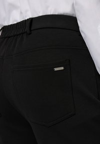 Pantaloni jogging neri con vita elastica, tasche laterali e una piccola etichetta metallica del marchio sulla tasca posteriore.
