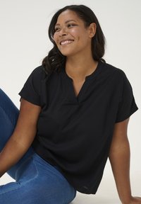Haut noir à manches courtes et décolleté en V. Tissu lisse, coupe décontractée. Porté avec un jean bleu ajusté. Design simple, sans motifs.