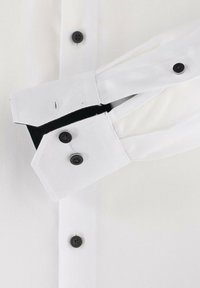 Weißes Hemd mit Knopfleiste und schwarzen Knöpfen, aus strukturiertem Stoff und mit kontrastierenden schwarzen Akzenten an den Manschetten. Die Manschetten sind mit eckigen Formen gestaltet.