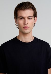 Tricou din bumbac negru, cu guler rotund și mâneci scurte, având un detaliu cu logo mic pe partea stângă a pieptului. Textură netedă, croială lejeră.