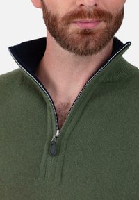 Pull vert foncé à fermeture éclair avec un col haut et une texture tricotée. Présente un col intérieur noir contrastant et un tirette de fermeture éclair en métal.