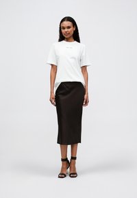 White short-sleeve t-shirt with a simple design, paired with a brown satin knee-length skirt, and black strappy sandals.