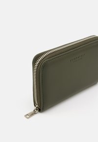 Olive green leather wallet featuring a silver zipper, rectangular shape, and embossed branding. Smooth texture with neat stitching details.