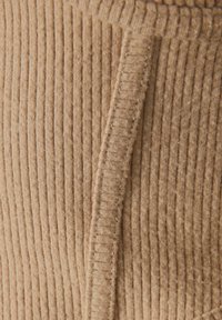 Gros plan sur un tissu beige côtelé avec une couture verticale, montrant la texture et les détails de la couture.