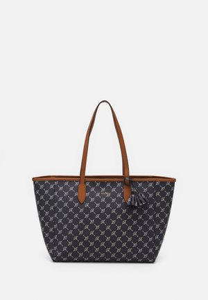 Sac cabas noir et marron avec un motif géométrique blanc répétitif, double poignée supérieure et détail de pompon sur une poignée.