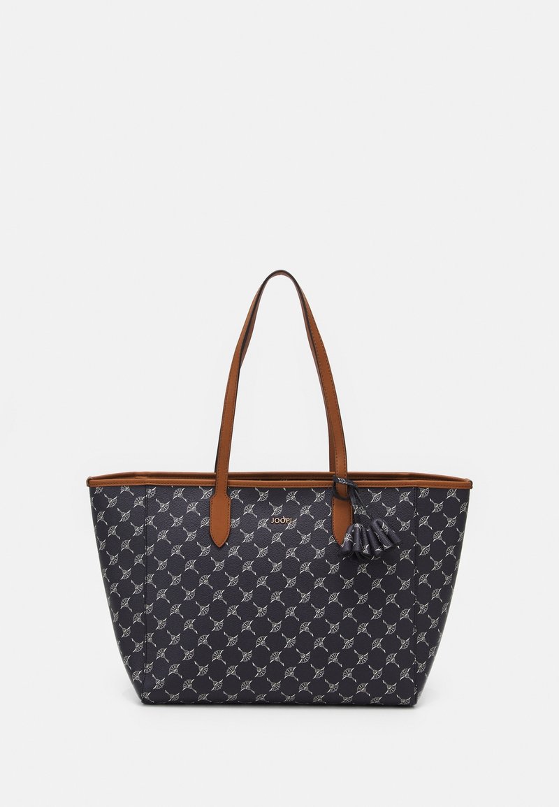 Sac cabas noir et marron avec un motif géométrique blanc répétitif, double poignée supérieure et détail de pompon sur une poignée.